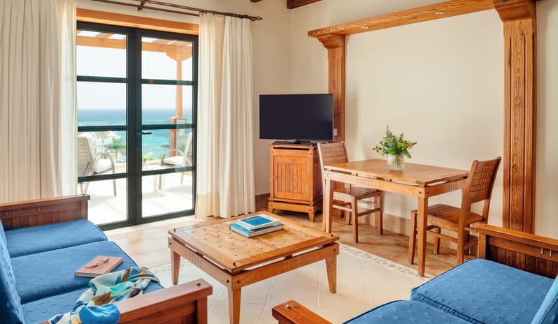 Junior Suite Sea View blue upholstered sofas, a wooden dining set, and glass doors opening to a sea-view balcony at Princesa Yaiza Suite Hotel Resort by Kenwood Travel