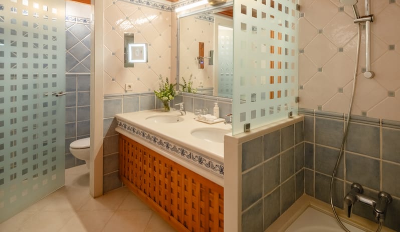 Junior Suite Sea View Bathroom double sink vanity with decorative blue tiles, a large mirror, and a walk-in shower with frosted glass partitions at Princesa Yaiza Suite Hotel Resort by Kenwood Travel