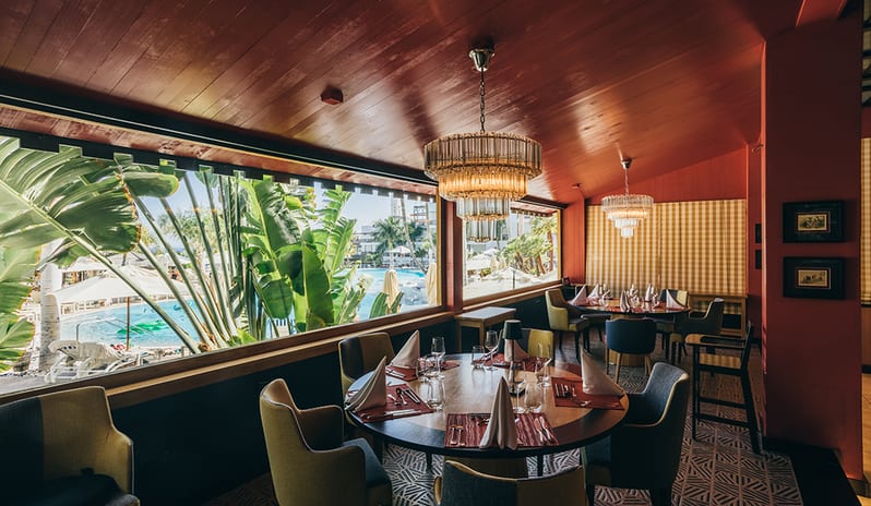 Round dining tables at Kampai Restaurant overlooking the resort pool and palm trees at Princesa Yaiza Suite Hotel Resort in Europe Holidays by Kenwood Travel