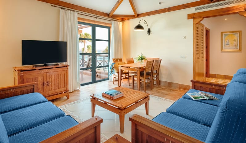 Suite Excellence Sea View traditional Canarian wood-beamed ceilings, blue sofas, a dining table, and large glass doors leading to a private balcony with sea viewsat Princesa Yaiza Suite Hotel Resort by Kenwood Travel