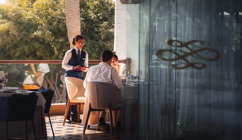 Professional waitress serving guests on the sunlit outdoor terrace of Isla de Lobos restaurant at Princesa Yaiza Suite Hotel Resort in Europe Holidays by Kenwood Travel
