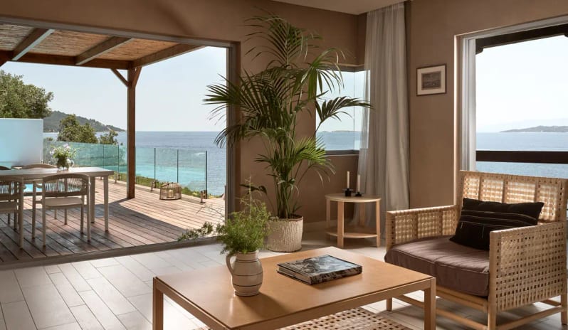 Bungalow Sea Front modern wicker lounge chair, wooden coffee table, and large sliding glass doors opening onto a private deck with a sea view at Eagles Palace by Kenwood Travel
