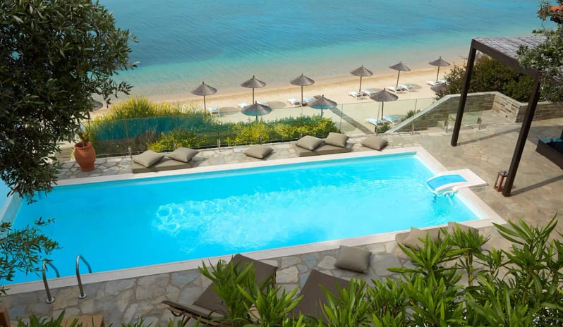 Presidential Bungalow tHigh-angle view of a private turquoise swimming pool at Eagles Palace Resort, positioned directly above a sandy beach with straw umbrellas and the blue ocean at Eagles Palace by Kenwood Travel