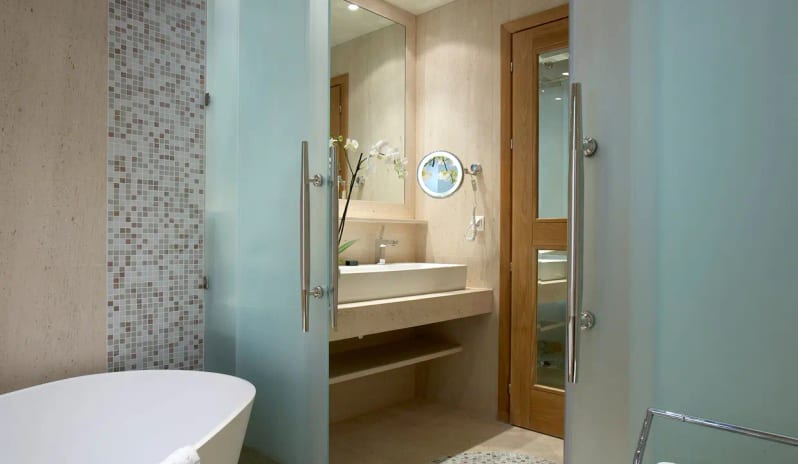 Presidential Bungalowbathroom in the Presidential Bungalow featuring a white freestanding soaking tub, frosted glass doors, a stone vanity with a vessel sink, and mosaic tile accents at Eagles Palace by Kenwood Travel