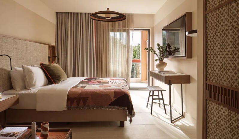 Deluxe Double Room Garden View bedroom at Eagles Resort in Halkidiki featuring warm earth tones, a private balcony with garden views, and contemporary wooden furniture at Eagles Palace by Kenwood Travel