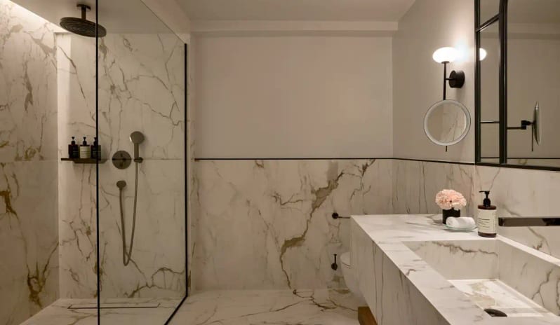 Deluxe Suite Garden View bathroom with floor-to-ceiling white marble, a spacious walk-in rainfall shower, and a minimalist stone vanity sink by Kenwood Travel