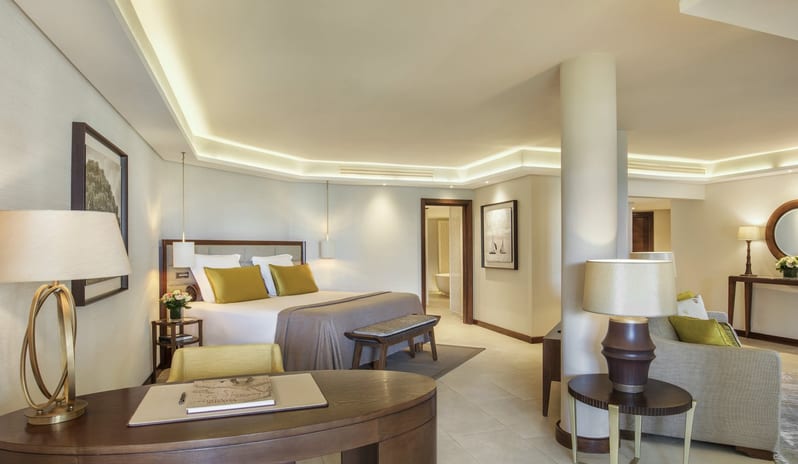 Palm Suite king-sized bed with lime green accent pillows, a dark wood curved desk with a designer lamp, and an open layout leading to a living area and bathroom at Royal Palm Beachcomber Luxury by Kenwood Travel