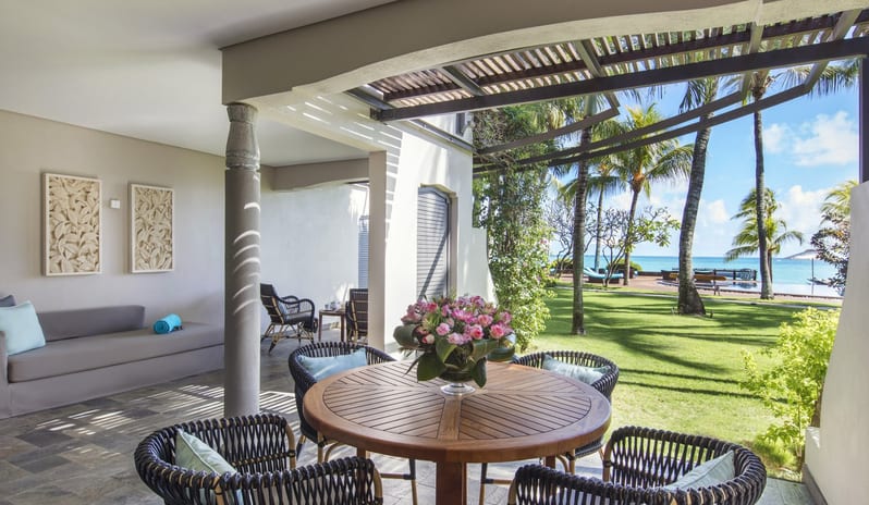 Palm Suite private terrace at a luxury beachfront resort, featuring a round wooden dining table with a bouquet of roses, comfortable wicker armchairs, and a lounge daybed at Royal Palm Beachcomber Luxury by Kenwood Travel