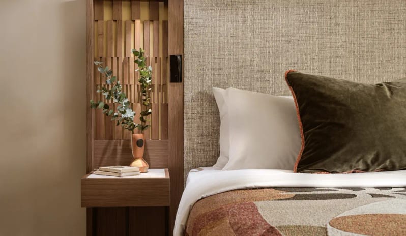 Deluxe Double Room Sea View bed with textured linen headboard, velvet pillows, and a floating wooden nightstand with a designer vase and integrated reading light at Eagles Palace by Kenwood Travel