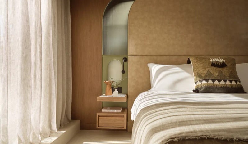 Panorama Suite Sea Front bedroom decor with warm earth tones, soft linen curtains, and a textured decorative pillow in a luxury Greek suite at Eagles Palace by Kenwood Travel