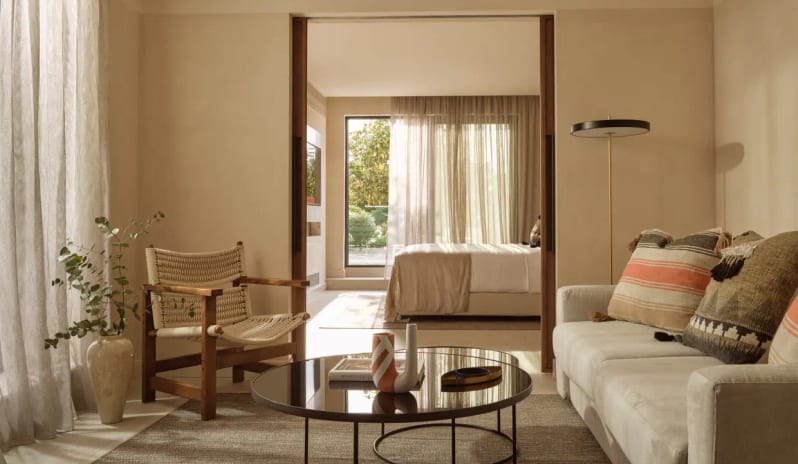 Panorama Suite Sea Frontshowcasing a minimalist sofa with textured pillows, a woven accent chair, and a view through sliding doors into the sunlit bedroom at Eagles Palace by Kenwood Travel