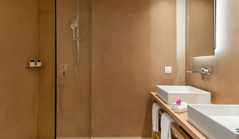 Bungalow Sea Front bathroom featuring earth-toned plaster walls, a walk-in glass shower, double vessel sinks on a wooden vanity, and fresh white towels at Eagles Palace by Kenwood Travel
