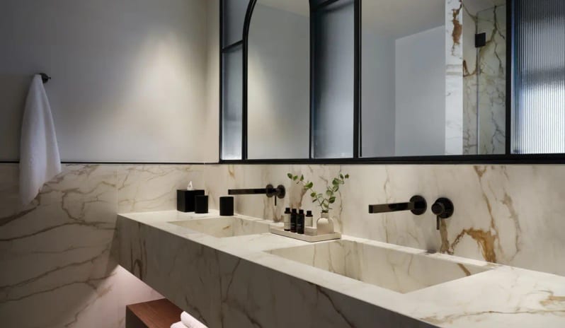 Deluxe Junior Suite Sea Front bathroom at Eagles Resort Halkidiki featuring a double marble vanity, matte black fixtures, and a large arched mirror at Eagles Palace by Kenwood Travel