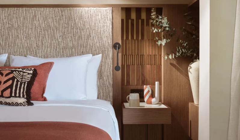 Deluxe Junior Suite Sea View custom wood-paneled headboard, floating nightstand with ceramic decor, and earth-toned Mediterranean textiles at Eagles Palace by Kenwood Travel