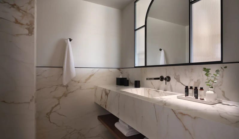 Deluxe Junior Suite Sea View Spa-style bathroom at Eagles Resort featuring a floating marble vanity, integrated stone sink, wall-mounted black faucets, and an arched mirror with frosted glass detail at Eagles Palace by Kenwood Travel