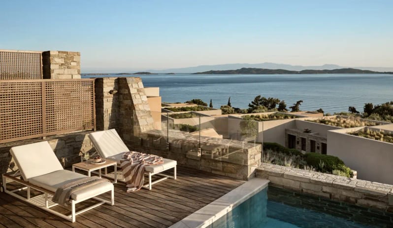 Ocean One Bedroom Pool Villa Sea View Private sun deck at Eagles Resort Halkidiki featuring white lounge chairs, a glass-walled infinity pool, and panoramic views of the Aegean Sea and Ammouliani Island at Eagles Villas by Kenwood Travel