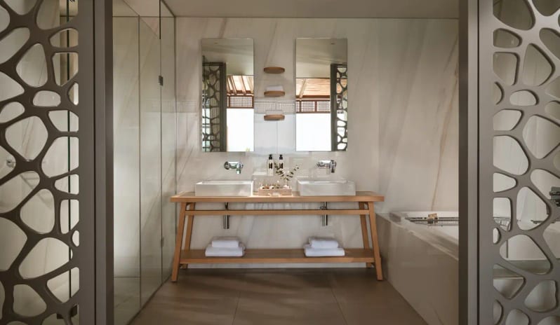 Ocean One Bedroom Pool Villa Sea View luxury bathroom at Eagles Resort Halkidiki featuring a wooden double vanity, marble walls, and contemporary glass shower at Eagles Villas by Kenwood Travel