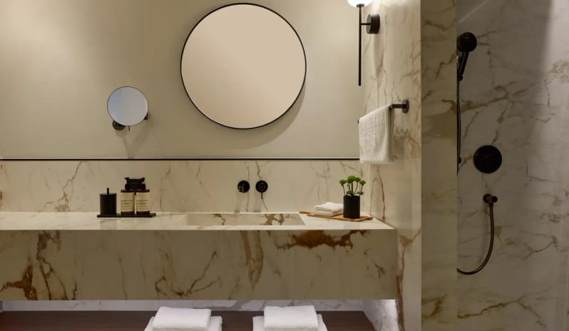 Panorama Suite Sea Front sleek, minimalist marble vanity with a recessed sink and round mirror, adjacent to a walk-in marble shower at Eagles Palace by Kenwood Travel