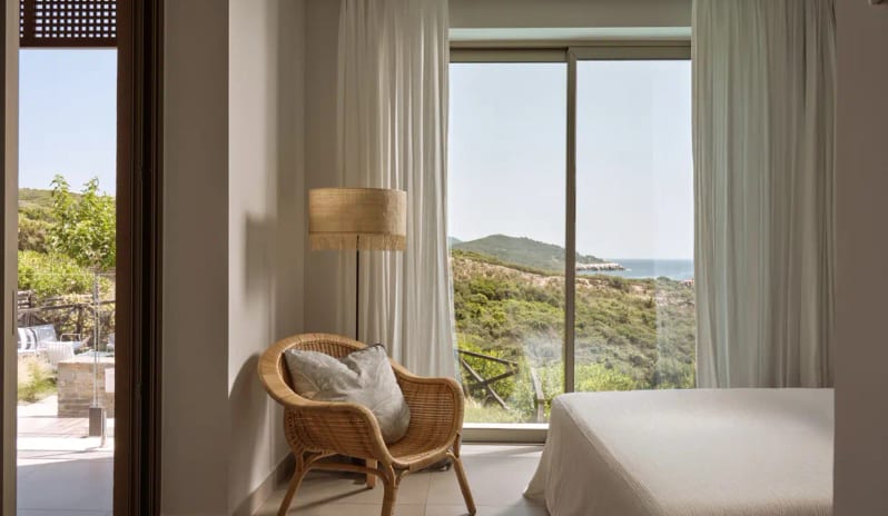 Residential 3 Bedroom Pool Villa Private Garden Sea View wicker armchair, floor lamp, and a large sliding glass door overlooking the Mediterranean coastline and lush green hills at Eagles Villas by Kenwood Travel