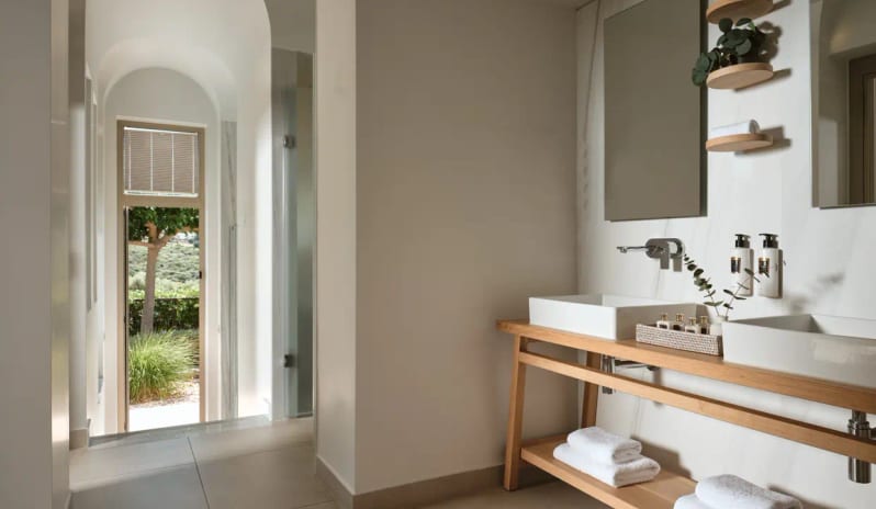Residential 2 Bedroom Pool Villa Sea View bathroom in a Halkidiki villa featuring a wooden double vanity with two vessel sinks, arched hallway, and a view of a private garden at Eagles Villas by Kenwood Travel