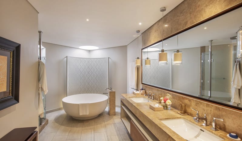 Penthouse Suite bathroom with a marble double vanity, large glass-enclosed walk-in shower, a freestanding soaking tub, and neutral stone tiling throughout at Royal Palm Beachcomber Luxury by Kenwood Travel