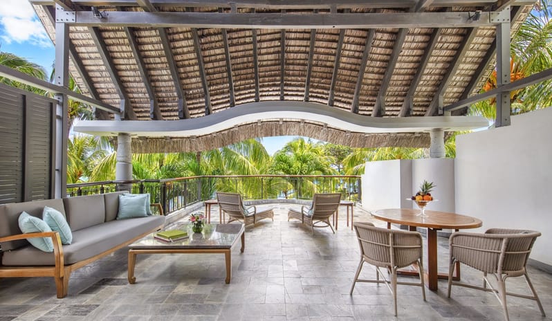 Penthouse Suite Beachcomber Luxury Penthouse Suite modern grey sofa, stone coffee table, wicker dining set, and lounge chairs overlooking lush palm trees at Royal Palm Beachcomber Luxury by Kenwood Travel