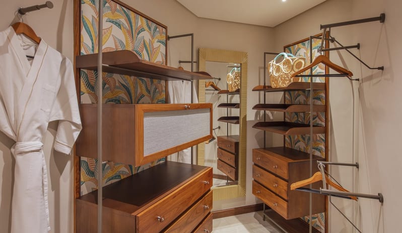 Penthouse Suite walk-in closet featuring warm wood cabinetry, built-in shelving, and drawers backed by vibrant tropical leaf wallpaper, complete with a gold-framed full-length mirror at Royal Palm Beachcomber Luxury by Kenwood Travel