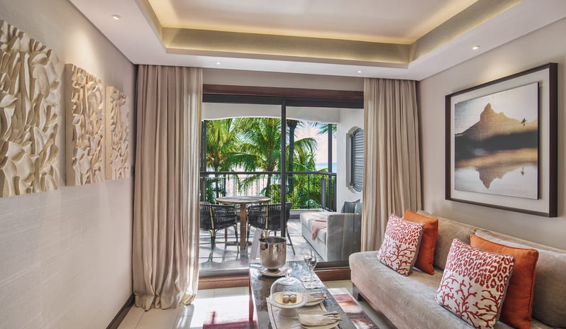 Junior Suite A wide-angle view of a luxury hotel suite featuring a king bed with vibrant orange bedding, a plush sofa with coral-patterned pillows, and a wooden writing desk at Royal Palm Beachcomber Luxury by Kenwood Travel