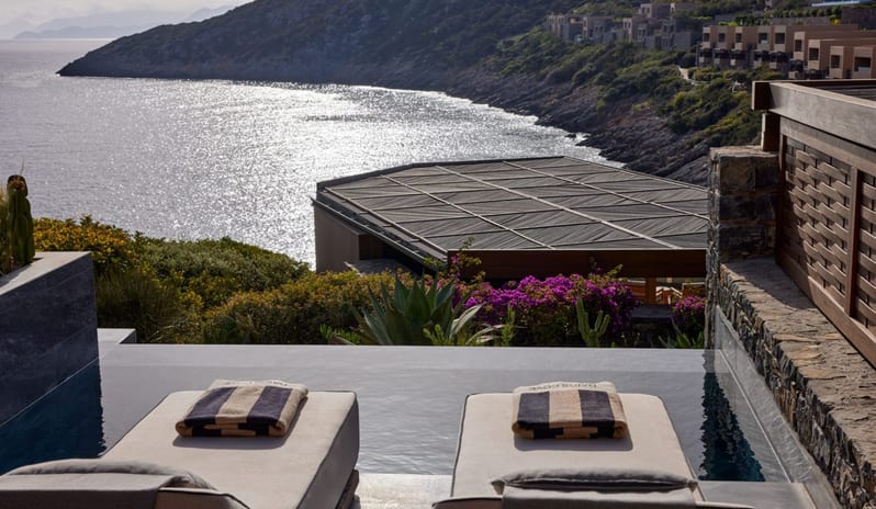 The Collection Junior Suite Sea View Private Pool private terrace sun lounger overlooking an infinity pool and the Mediterranean coastline with sparkling blue water and rugged hills at Daios Cove by Kenwood Travel