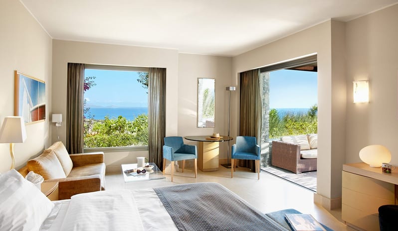 The Collection Premium Junior Suite with Private Pool large bed, seating area, and floor-to-ceiling glass doors opening to a balcony with a Mediterranean sea view at Daios Cove by Kenwood Travel