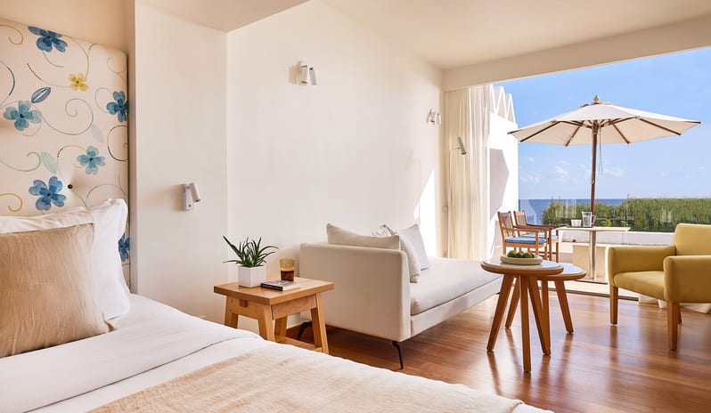 Classic Junior Suite Sea View white sofa, modern wood flooring, and a private balcony with an ocean view and patio seating at St. Nicolas Bay Resort by Kenwood Travel