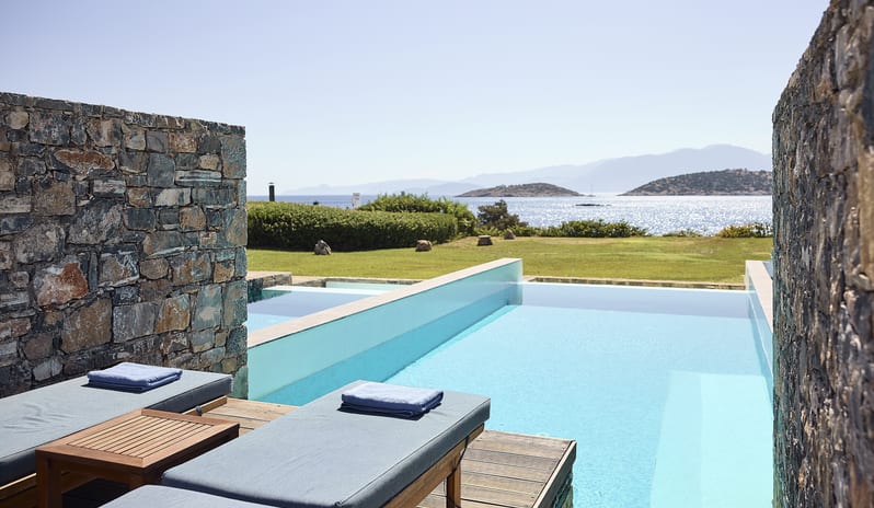 Classic Studio Private Pool Sea View marble-top wooden coffee tables and a potted succulent, with a sun-drenched private terrace and blue sea in the background at St. Nicolas Bay Resort by Kenwood Travel