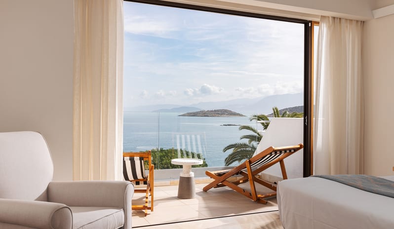 Classic Suite One bedroom opening to a private balcony with sun loungers and mountain-sea vistas at St. Nicolas Bay Resort by Kenwood Travel