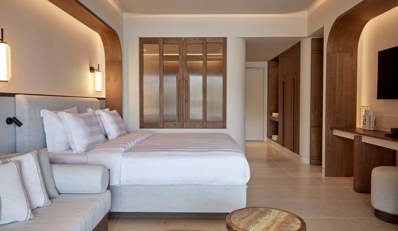 The Collection Two Bedroom Suite Sea View Private Pooll built-in wooden arches, integrated warm LED lighting, a plush grey sofa, and a minimalist desk area with marble-topped coffee tables at Daios Cove by Kenwood Travel