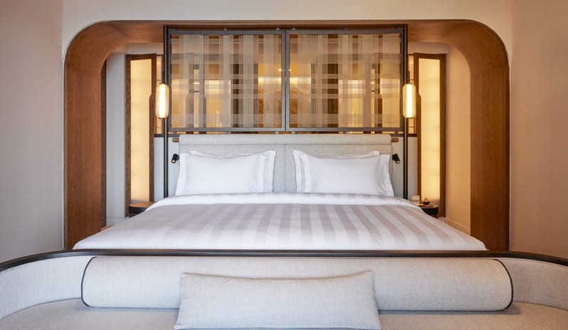 The Collection Two Bedroom Suite Sea View Private Pooll king-size bed with striped linens, integrated wooden archway, and decorative woven screen headboard with warm pendant lighting at Daios Cove by Kenwood Travel