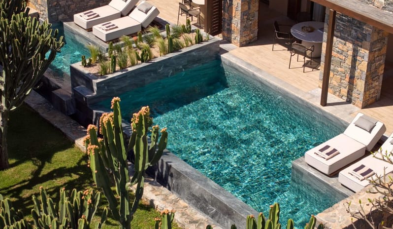 The Collection Two Bedroom Suite Sea View Private Pooll infinity pool surrounded by stone walls, sun loungers, and lush green cacti, overlooking a coastal landscape at Daios Cove by Kenwood Travel
