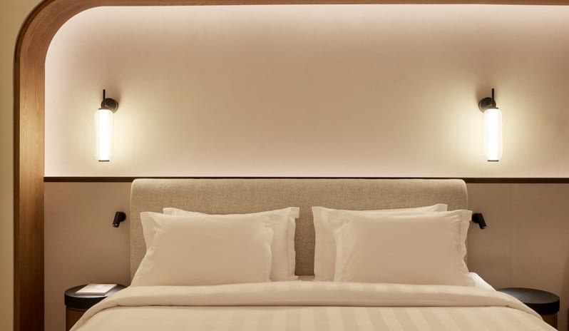 The Collection Junior Suite Sea View bedroom with a wood-framed bed nook, glowing wall lamps, and white striped bedding at Daios Cove by Kenwood Travel