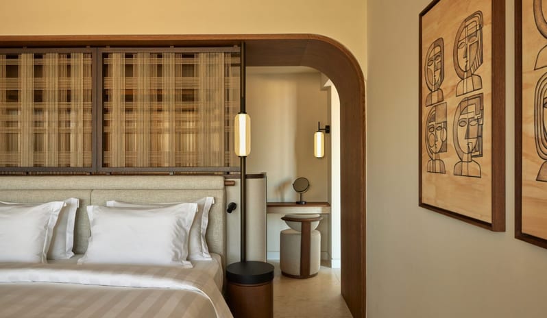 The Collection One bedroom Suite Sea View Private Pool arched wood-lined entryway leading to a vanity desk, a modern bedside pendant light, and framed line art on the wall at Daios Cove by Kenwood Travel