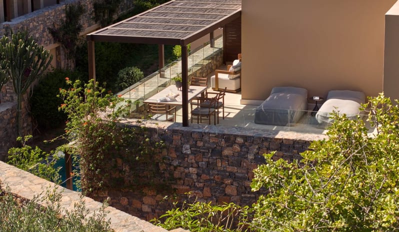 The Collection One bedroom Suite Sea View Private Pool private stone terrace at a luxury resort featuring a wooden pergola-covered dining area, sun loungers, and lush Mediterranean greenery at Daios Cove by Kenwood Travel