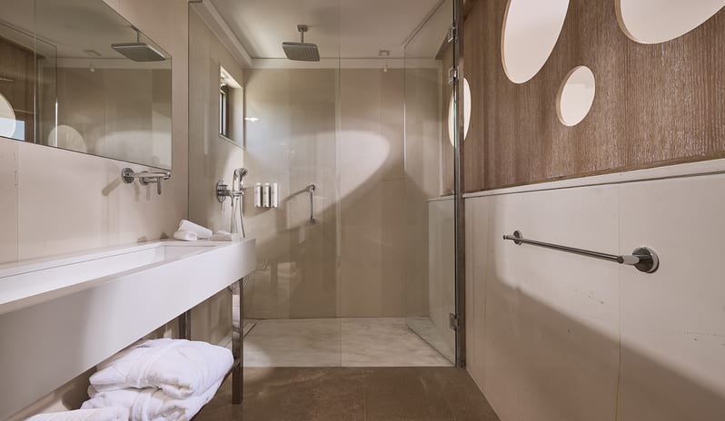 Olives & Sea Two Bedroom Suite Private Pool Harbour View/Sea View bathroom at Olives & Sea featuring a glass-enclosed walk-in rainfall shower, a long white trough sink, and stone-tiled walls at St.Nicolas Bay Resort by Kenwood Travel