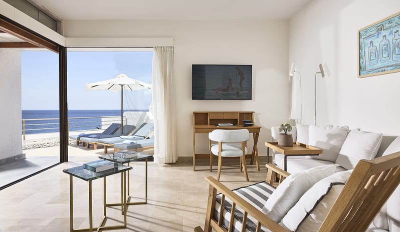 Club Suite One Bedroom Private Pool Sea View living area with a white sofa, a wooden writing desk, and a striped rocking chair opening onto a private balcony with sunbeds and sea views at St.Nicolas Bay Resort by Kenwood Travel