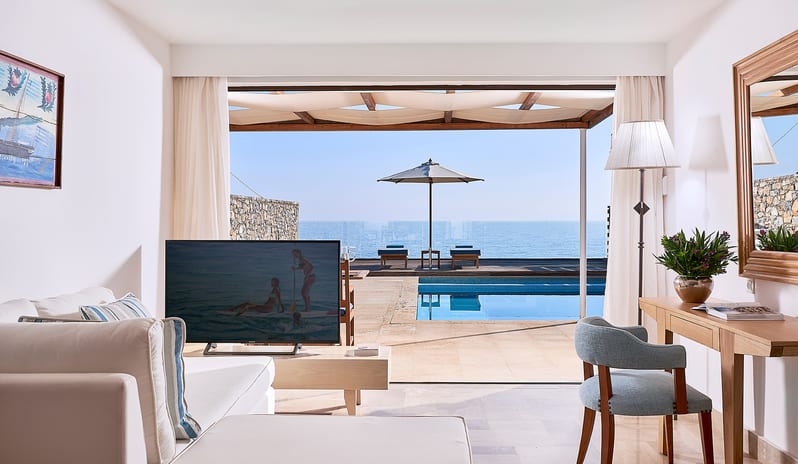 Club Suite One Bedroom Private Pool Sea View living area featuring a white sofa, a wooden work desk with a blue chair, and large glass doors opening to a private pool and the ocean at St.Nicolas Bay Resort by Kenwood Travel
