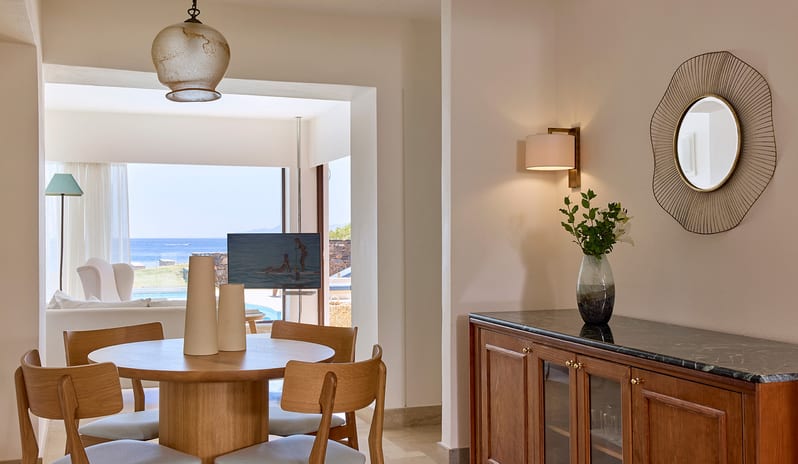 Club Suite One Bedroom Private Pool Sea View dining area within a club suite featuring a round wooden table, marble-top sideboard, and a view through to the living area and sea at St.Nicolas Bay Resort by Kenwood Travel