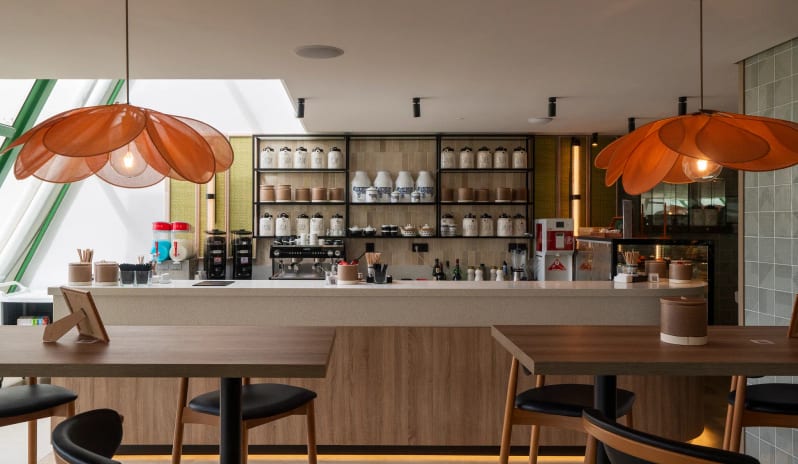 Coco Cafe interior featuring large orange flower-shaped pendant lights, wooden bar counter, and shelves filled with white ceramic jars at Dreams Lanzarote Playa Dorada Resort & Spa by Kenwood Travel