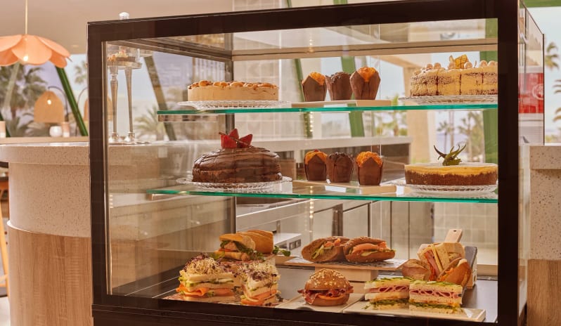 Coco Cafe A glass display case in a cafe filled with gourmet chocolate cakes, muffins, and various fresh sandwiches and wraps at Dreams Lanzarote Playa Dorada Resort & Spa by Kenwood Travel