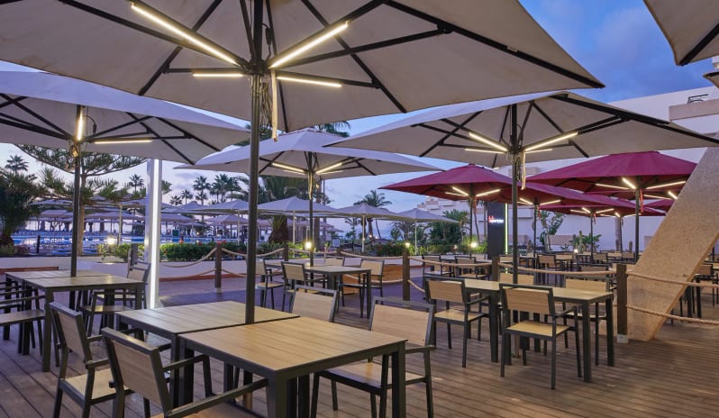 Barefoot Grill modern wooden tables with turquoise chairs, patterned wallpaper with food icons, and a bright buffet service counter at Dreams Lanzarote Playa Dorada Resort & Spa by Kenwood Travel