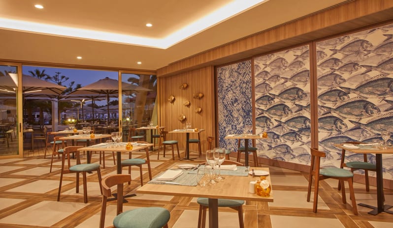 Bluewater Grill findoor dining room at a luxury resort with contemporary decor, warm lighting, and a view of the outdoor patio at Dreams Lanzarote Playa Dorada Resort & Spa by Kenwood Travel