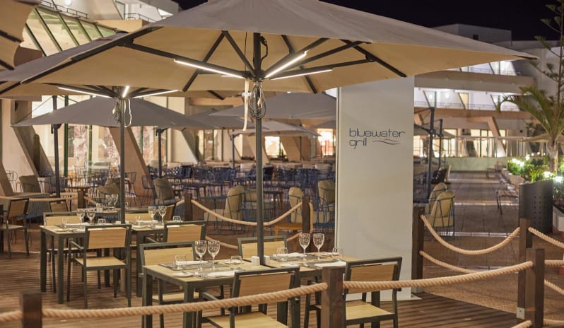 Bluewater Grill featuring wooden tables, modern chairs, and large lighted umbrellas on a deck at Dreams Lanzarote Playa Dorada Resort & Spa by Kenwood Travel