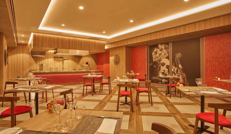 Himitsu Interior of a modern Japanese restaurant featuring warm wood-paneled walls, minimalist wooden tables with red cushioned chairs at Dreams Lanzarote Playa Dorada Resort & Spa by Kenwood Travel