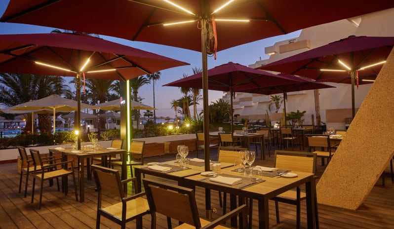 Himitsu featuring wooden decking, modern dining tables, and large red patio umbrellas with integrated LED lighting at Dreams Lanzarote Playa Dorada Resort & Spa by Kenwood Travel